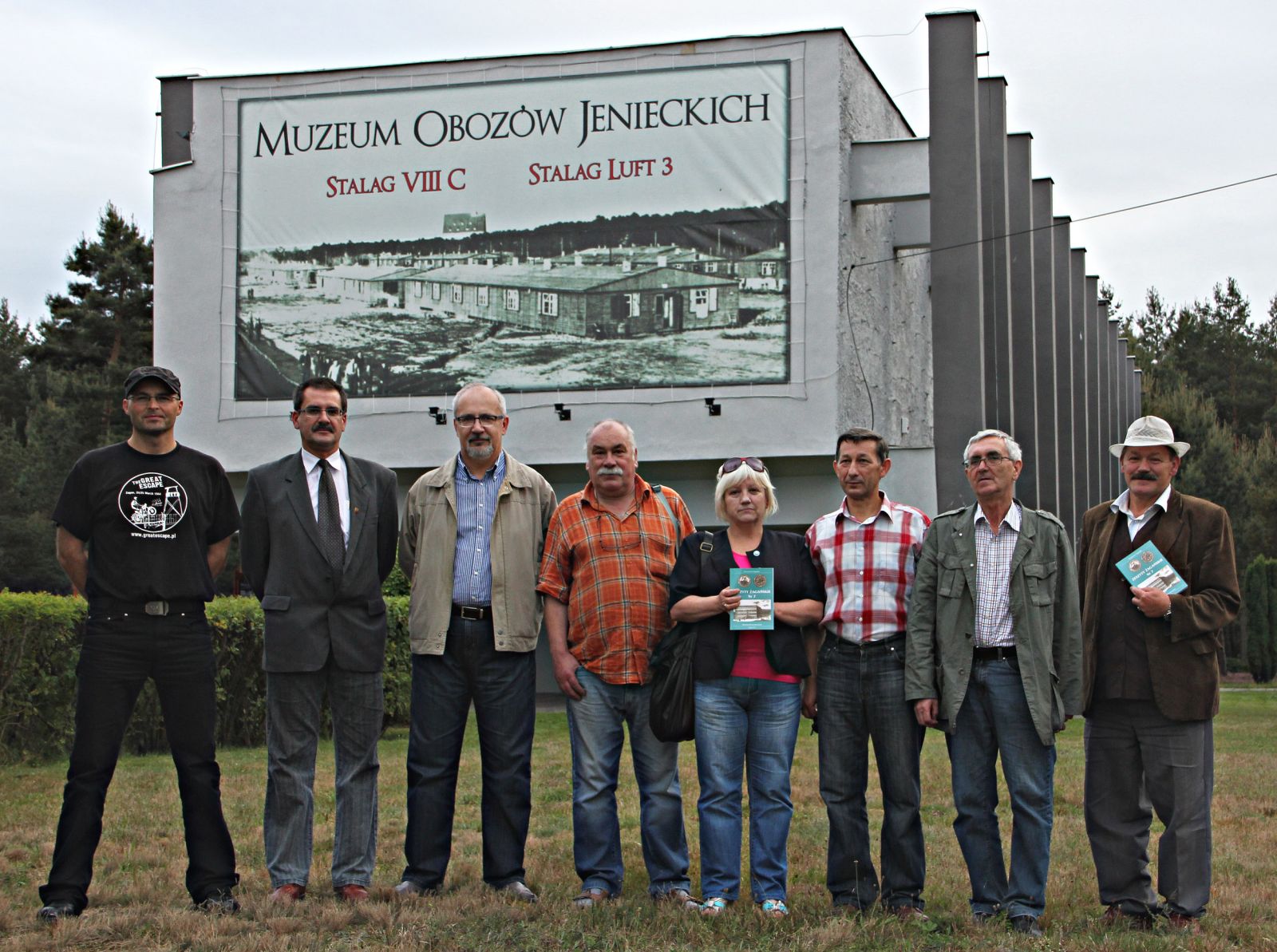 Na tle Muzeum Obozów Jenieckich w Żaganiu pozują członkowie kolegium redakcyjnego Zeszytów Żagańskich, siedmiu mężczyzn i jedna kobieta. 